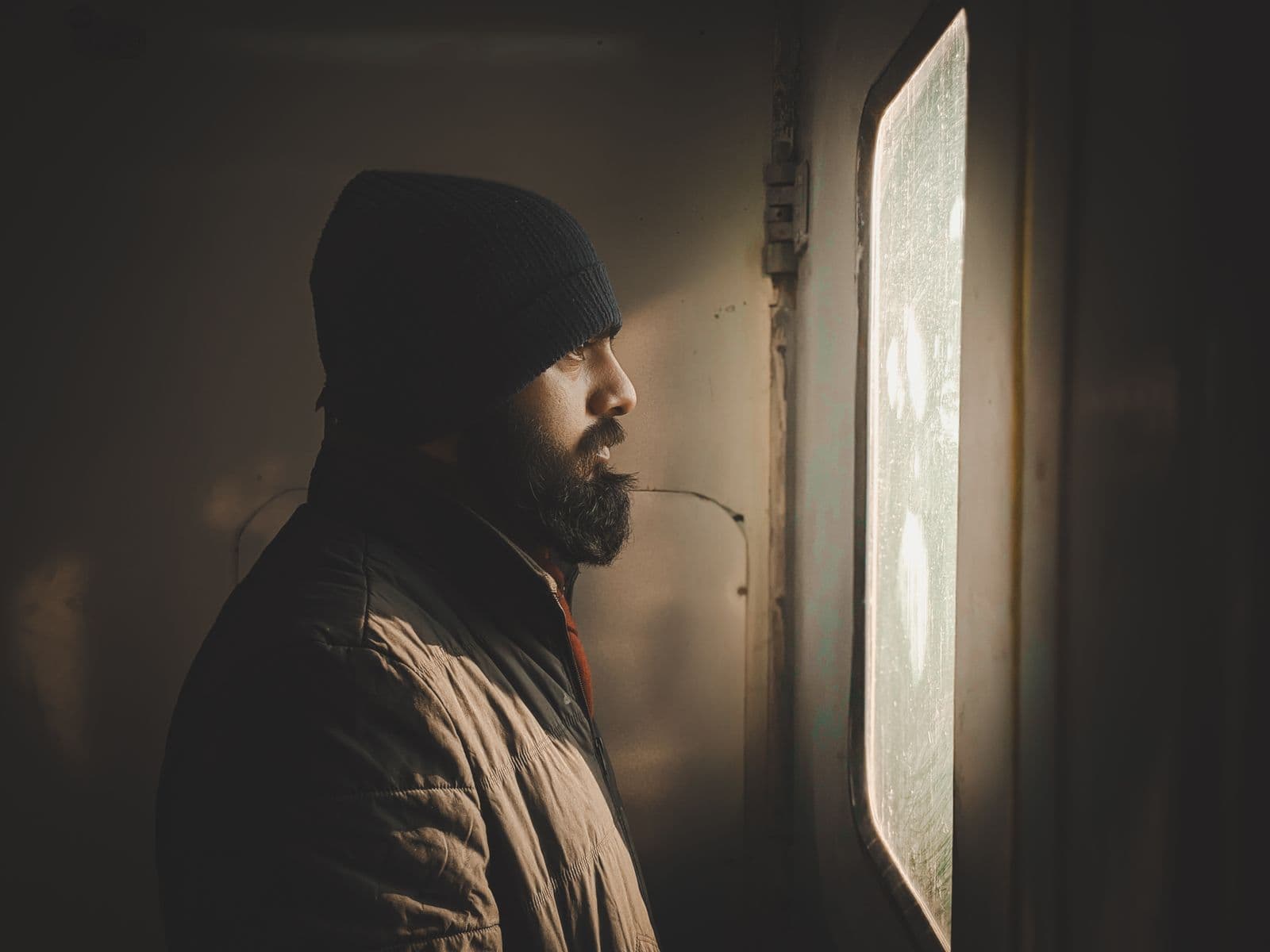 A man looking thoughtfully out of a window in warm light, lost in reflection