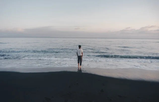 A person standing quietly at the shoreline, looking out to sea