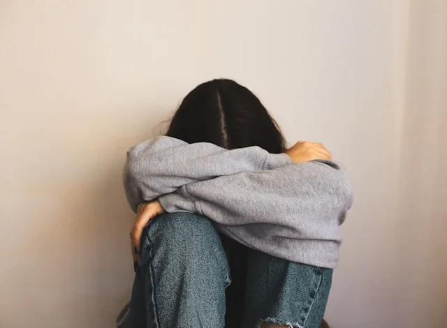 A person sitting curled up against a wall with their head down, feeling the quiet loneliness after a breakup