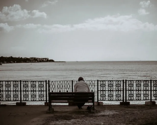 A lone figure sitting on a bench facing the sea — the quiet reality behind the loneliness epidemic