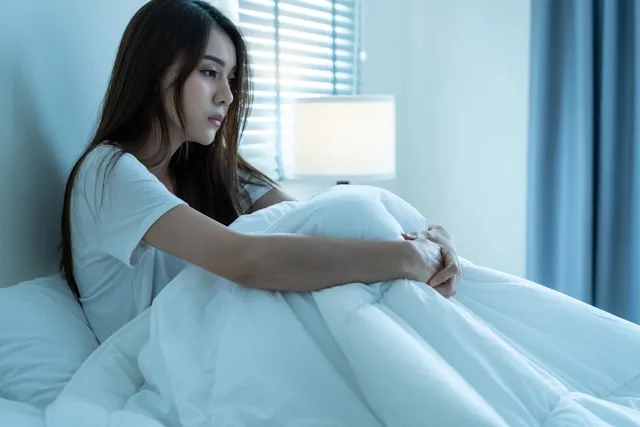A woman sitting awake alone in bed at night, lit by a lamp — the quiet loneliness that draws people to AI companions