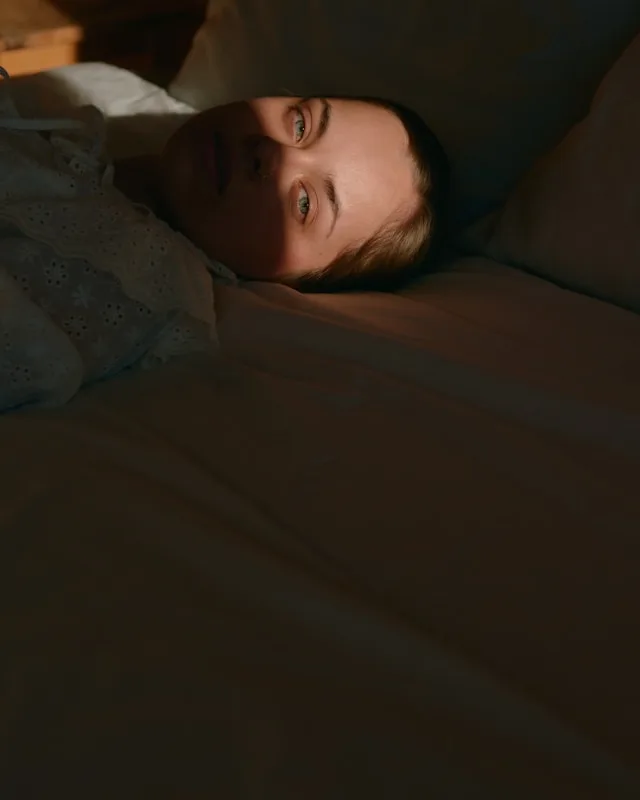 A person lying awake in a dark bedroom, eyes open, unable to switch off