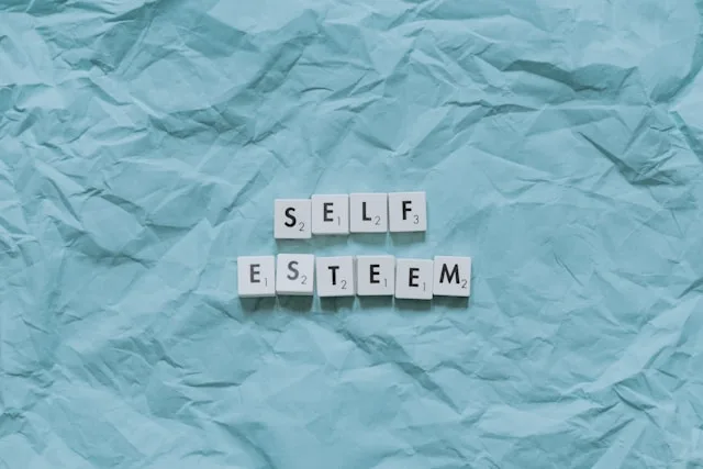 Letter tiles spelling the words self esteem on a plain background
