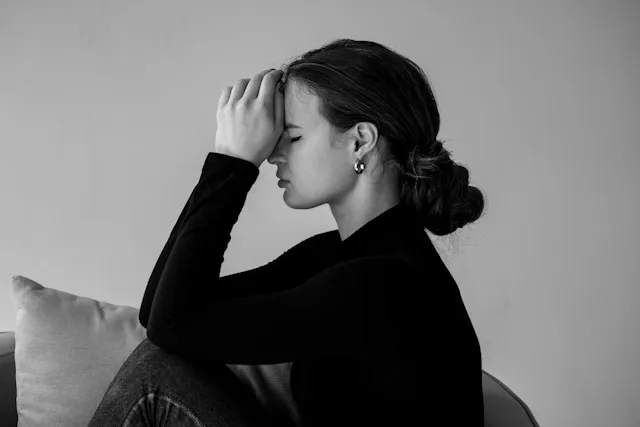A person sitting quietly with a hand to their forehead, eyes closed, working through racing thoughts before sleep