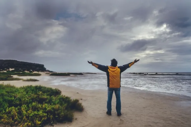 A person standing on a beach with arms open to the sky, adjusting to a new chapter